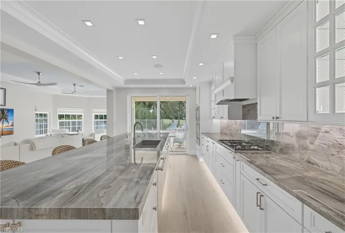 Kitchen featuring white cabinets, a tray ceiling, tasteful backsplash, a large island, and light wood-type flooring