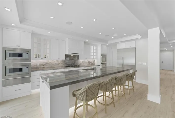 Kitchen with a tray ceiling, white cabinetry, a breakfast bar area, backsplash, and recessed lighting