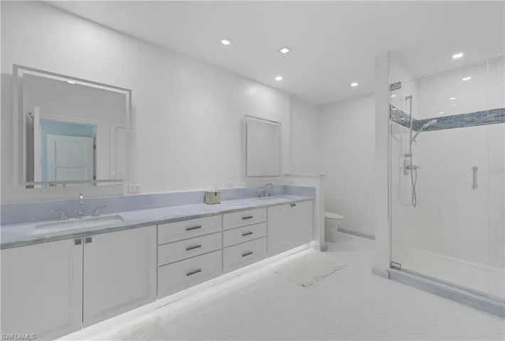 Bathroom featuring a shower stall, double vanity, and recessed lighting