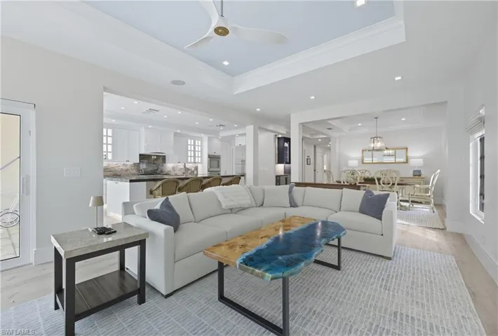 Living room with a tray ceiling, light wood-type flooring, crown molding, ceiling fan, and recessed lighting