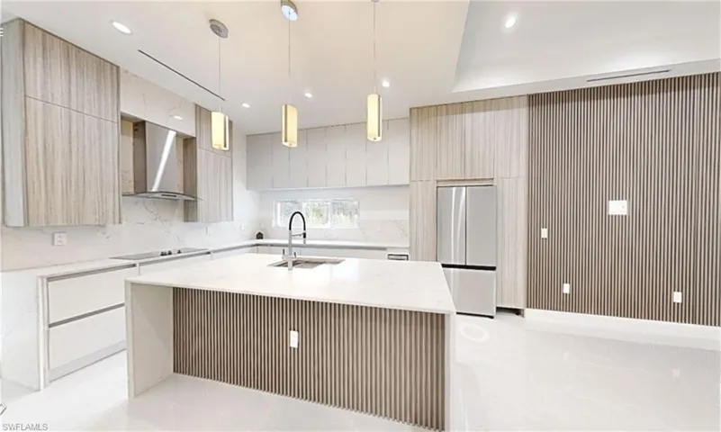 Kitchen with wall chimney exhaust hood, modern cabinets, stainless steel refrigerator, a sink, and black electric stovetop