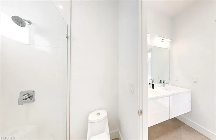 Bathroom featuring toilet, a sink, a stall shower, double vanity, and baseboards