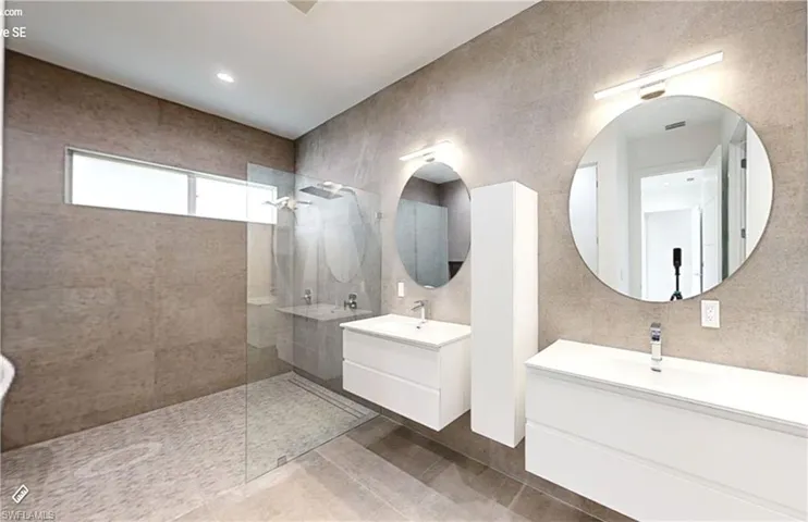 Full bath featuring two vanities, a sink, and walk in shower