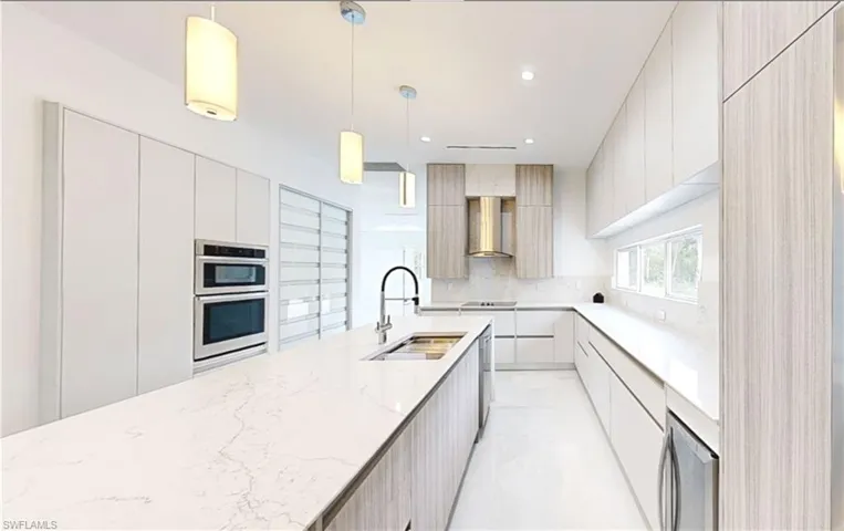 Kitchen featuring wall chimney range hood, stainless steel double oven, modern cabinets, and a sink