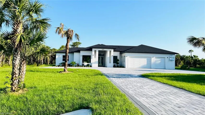 Prairie-style home featuring a garage, stucco siding, a front yard, and decorative driveway