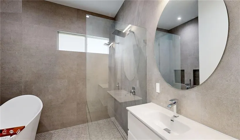 Full bathroom featuring a walk in shower, a freestanding tub, vanity, and tile walls