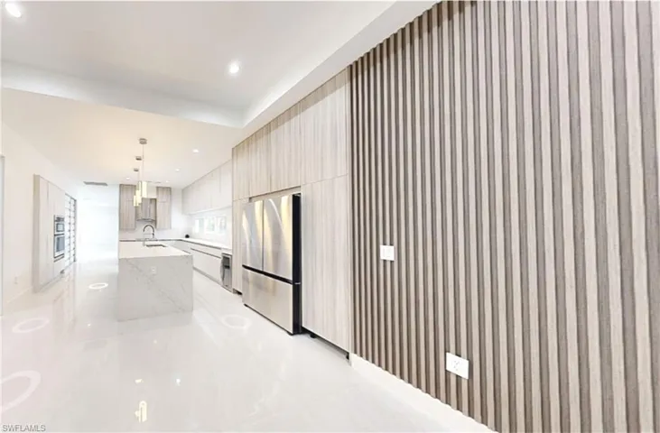 Kitchen with wall chimney range hood, an island with sink, freestanding refrigerator, modern cabinets, and a sink