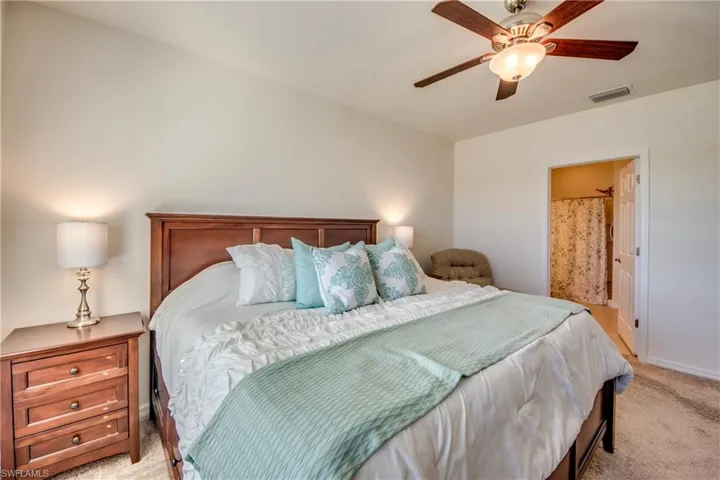 Carpeted bedroom with connected bathroom and ceiling fan