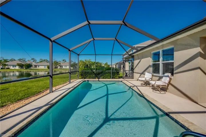 View of swimming pool with a patio,screen enclosure, a lawn, and a water view