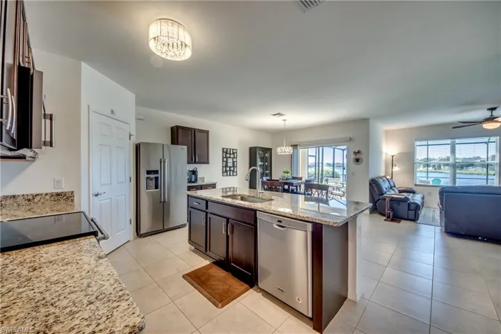 Kitchen with decorative light fixtures, ceiling fan with notable chandelier, an island with sink, appliances with stainless steel finishes, and sink