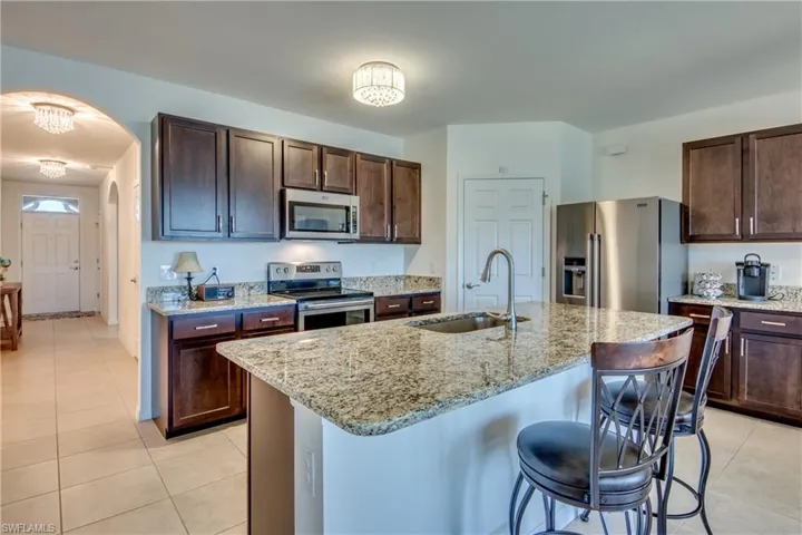 Kitchen featuring stainless steel appliances, sink, light tile floors, and a kitchen island with sink