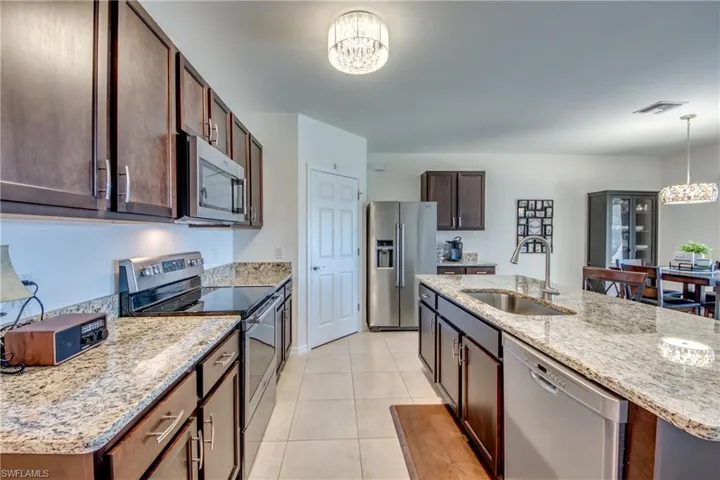 Kitchen featuring an inviting chandelier, appliances with stainless steel finishes, decorative light fixtures, sink, and light tile floors