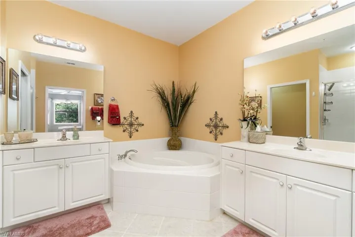 Primary ensuite bath featuring a shower, garden tub, two vanities, and light tile flooring.
