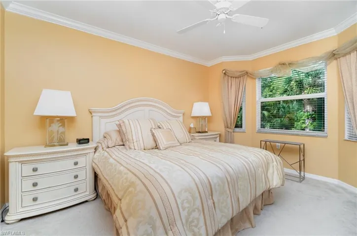 Bedroom with dresser with mirror, TV mounted to the wall, light carpet, crown molding, ceiling fan and adjoining bathroom.