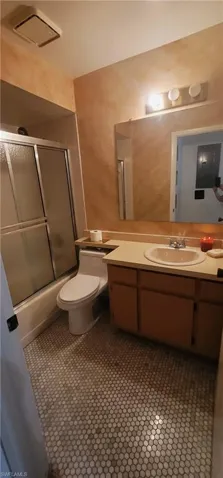 Full bath with vanity, enclosed tub / shower combo, a textured wall, and tile patterned floors