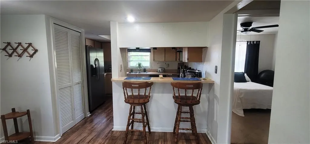Kitchen with stainless steel refrigerator with ice dispenser, a peninsula, dark wood finished floors, a kitchen breakfast bar, and ceiling fan