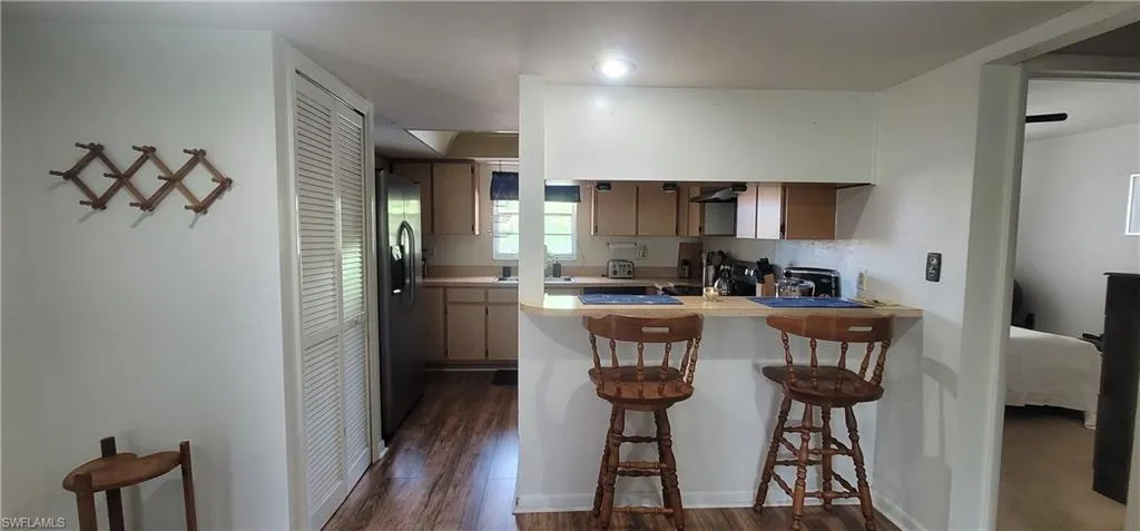 Kitchen with stainless steel fridge with ice dispenser, a peninsula, light countertops, and dark wood-style flooring