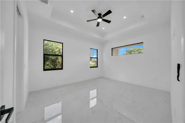 Spare room featuring a tray ceiling, marble finish floors, recessed lighting, and a ceiling fan