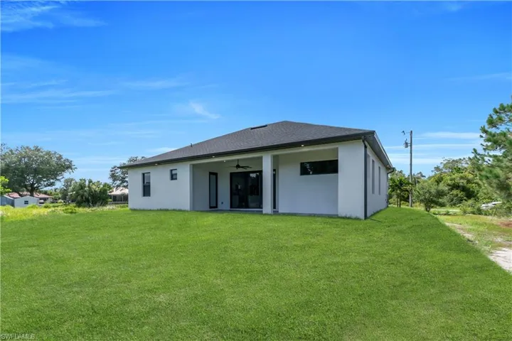 Rear view of house featuring ceiling fan, a lawn, and stucco siding