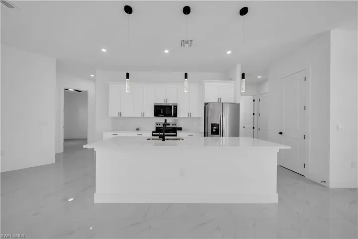 Kitchen with a center island with sink, light marble finish flooring, stainless steel appliances, white cabinetry, and light countertops
