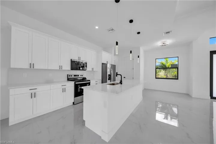Kitchen with light marble finish floors, stainless steel appliances, white cabinetry, a center island with sink, and recessed lighting