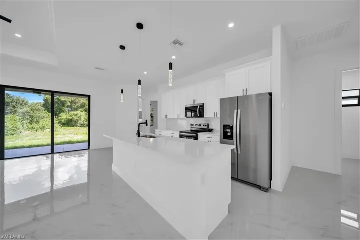 Kitchen featuring appliances with stainless steel finishes, light marble finish floors, white cabinets, a center island with sink, and recessed lighting