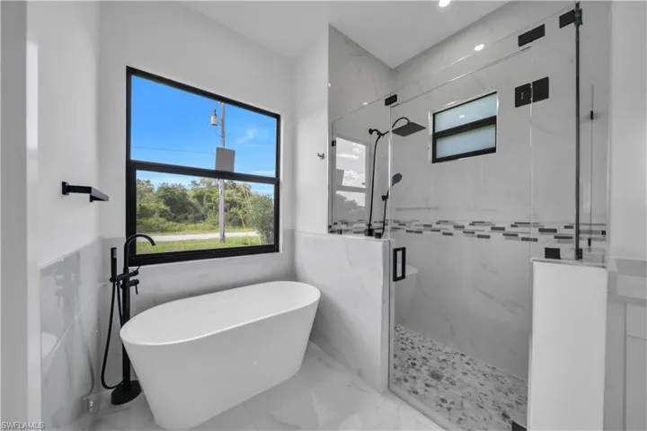 Full bath with a freestanding bath, a marble finish shower, tile walls, marble finish floors, and a wainscoted wall