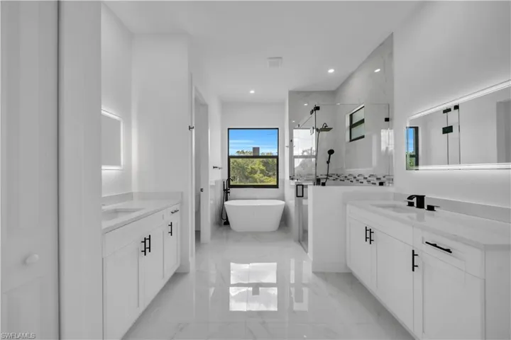 Full bathroom with a stall shower, marble tiled flooring, two vanities, a freestanding tub, and recessed lighting