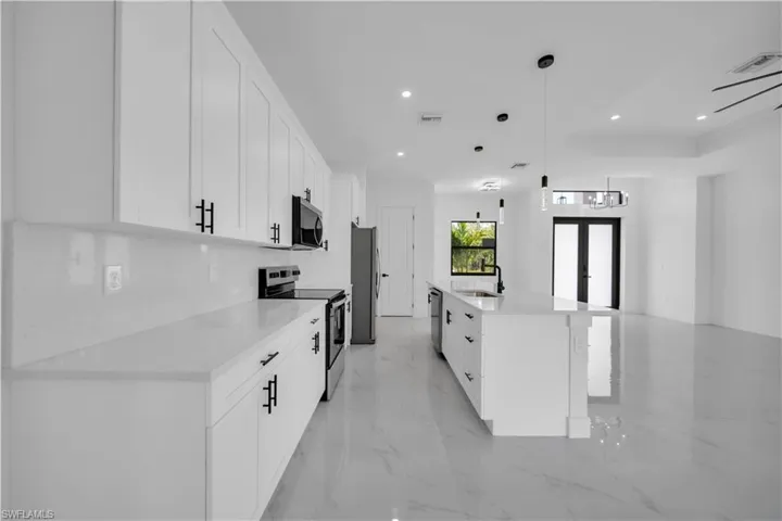 Kitchen featuring appliances with stainless steel finishes, white cabinetry, a center island with sink, light marble finish flooring, and recessed lighting