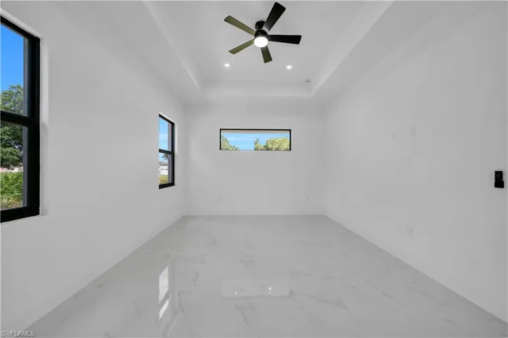 Spare room featuring marble finish flooring, a tray ceiling, ceiling fan, crown molding, and recessed lighting