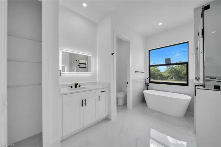 Bathroom featuring vanity, a freestanding tub, marble tiled flooring, a walk in closet, and recessed lighting