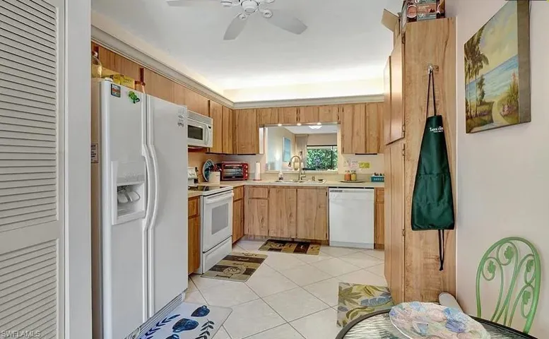 Kitchen featuring white appliances, light countertops, light tile patterned floors, a ceiling fan, and light wood finish cabinetry