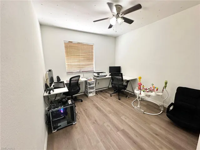 Home office with light wood-style floors, a ceiling fan, and a textured wall