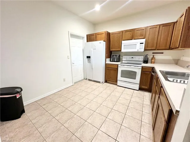 Kitchen featuring light countertops, white appliances, wood finish cabinetry, and light tile patterned floors