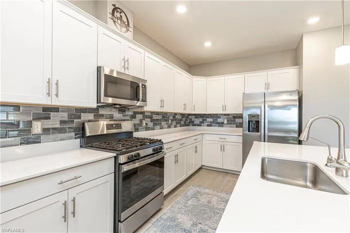 Kitchen featuring a sink, tasteful backsplash, white cabinetry, stainless steel appliances, and light countertops