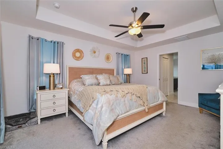 Carpeted bedroom featuring a tray ceiling with a ceiling fan