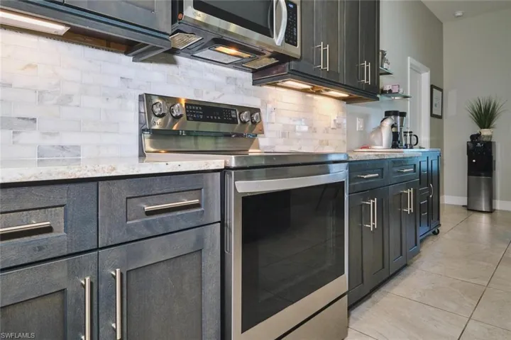 Modern kitchen featuring stainless steel appliances, dark wood-finish cabinetry, light-toned countertops, a subway tile backsplash, and recessed lighting