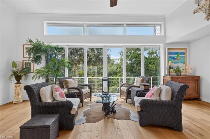Vaulted ceiling with an exposed wood beam, large transom windows, full-height sliding glass doors, and wood-finish flooring