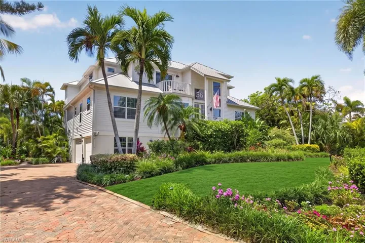White multi-story residence featuring a balcony, attached garages, and a brick paver driveway