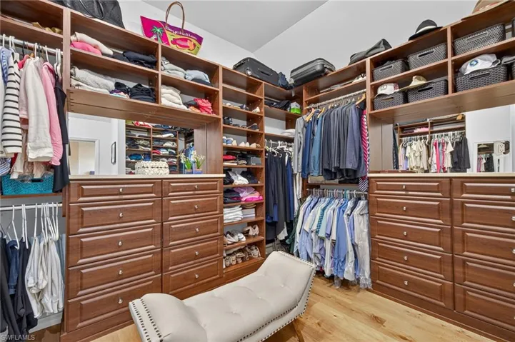 Custom closet system featuring wood-finish cabinetry, integrated shelving, ample hanging storage, and wood-finish flooring