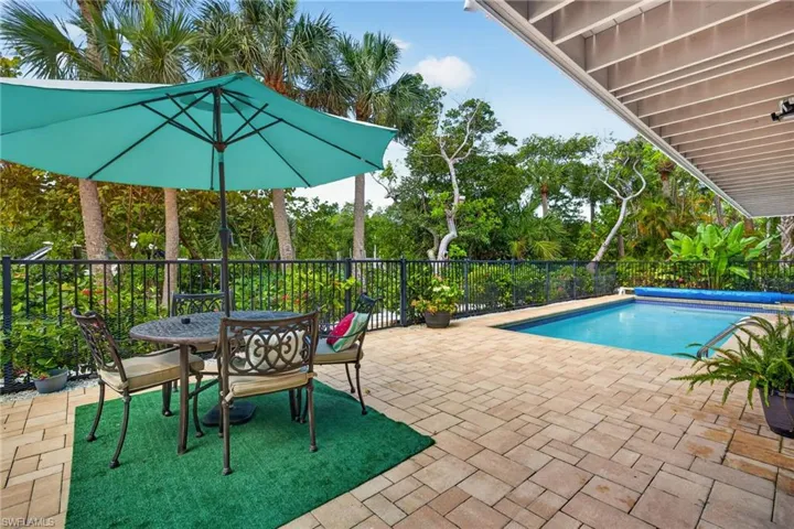 Paver patio with an in-ground swimming pool, surrounded by a black metal fence and mature trees