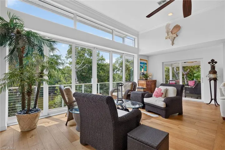 High ceilings with crown molding, wood-finish flooring, a ceiling fan, and extensive glass doors with transom windows