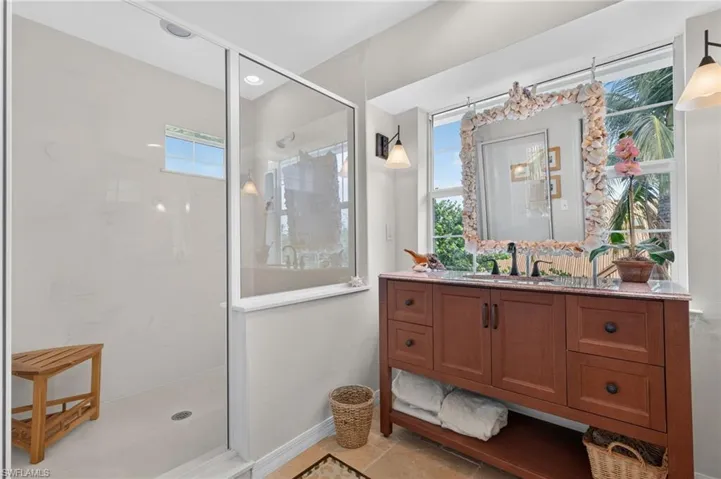 Glass-enclosed shower with white tiled walls, wood-finish vanity with countertop, and dual windows