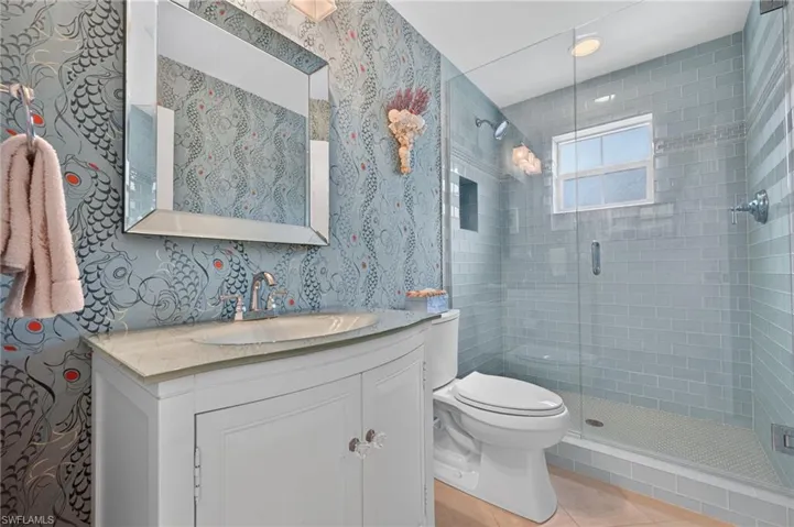 Vanity with integrated sink and chrome faucet, framed mirror, glass-enclosed shower with subway tile surround, recessed shower niche, and mosaic tile shower pan