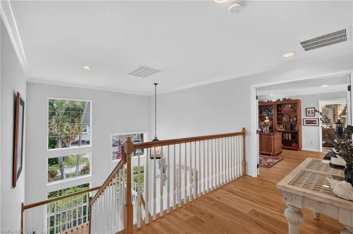 Hardwood flooring, white painted walls, crown molding, a wood and white spindle staircase, and multiple windows