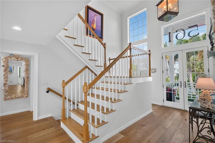 Hardwood flooring, wood-finish staircase with white risers, double entry doors with glass panels, high ceilings, and transom windows