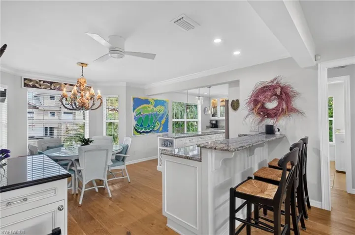 Wood-finish flooring throughout, white cabinetry with dark countertops, breakfast bar with a granite countertop, recessed lighting, and a decorative chandelier