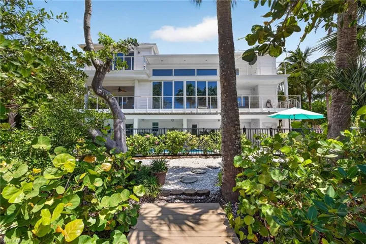 Two-story residence featuring extensive glazing and multiple balconies, set amidst tropical foliage