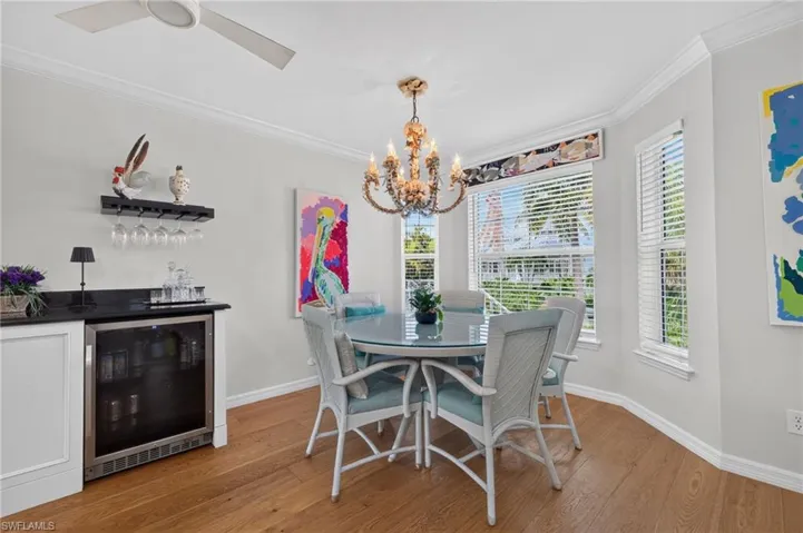 Recessed beverage cooler, built-in cabinetry, dark countertop, wood-finish flooring, and crown molding