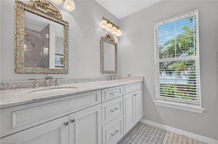 Dual vanity with undermount sinks, stone countertop, two framed mirrors, and wall-mounted lighting